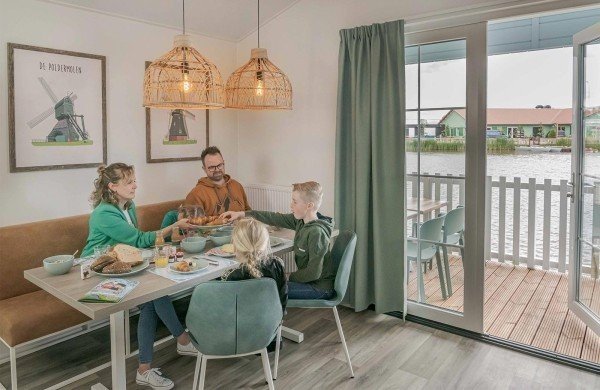 Een gezin die aan het eten is in &eacute;&eacute;n van de accommodaties die aan het water ligt op ons kindvriendelijk vakantiepark.